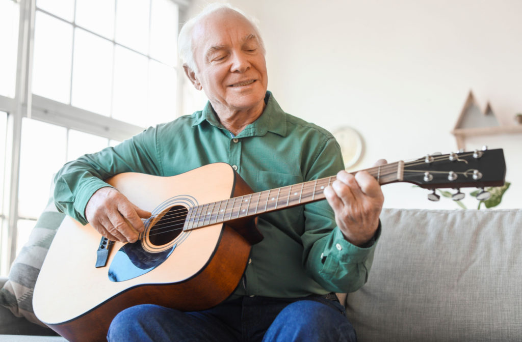 A senior man sitting on a couch and playing a guitar