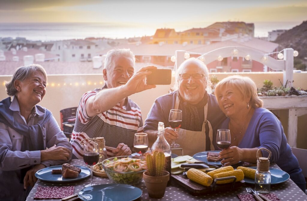 Two senior couples having dinner together snap a selfie of the sunset behind them