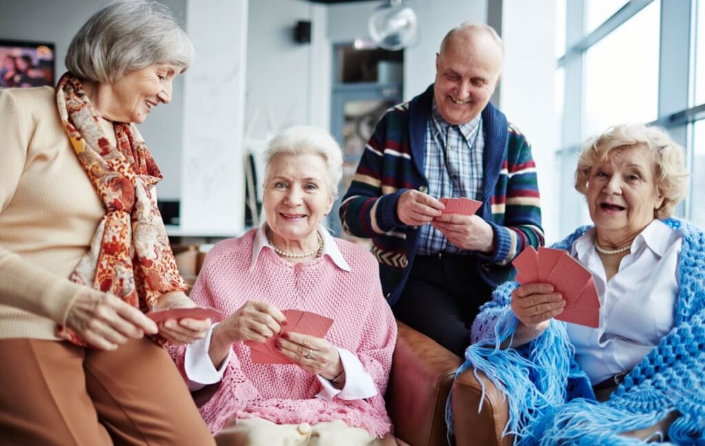 A group of seniors sit together and play cards in the recreation room at their senior living community.