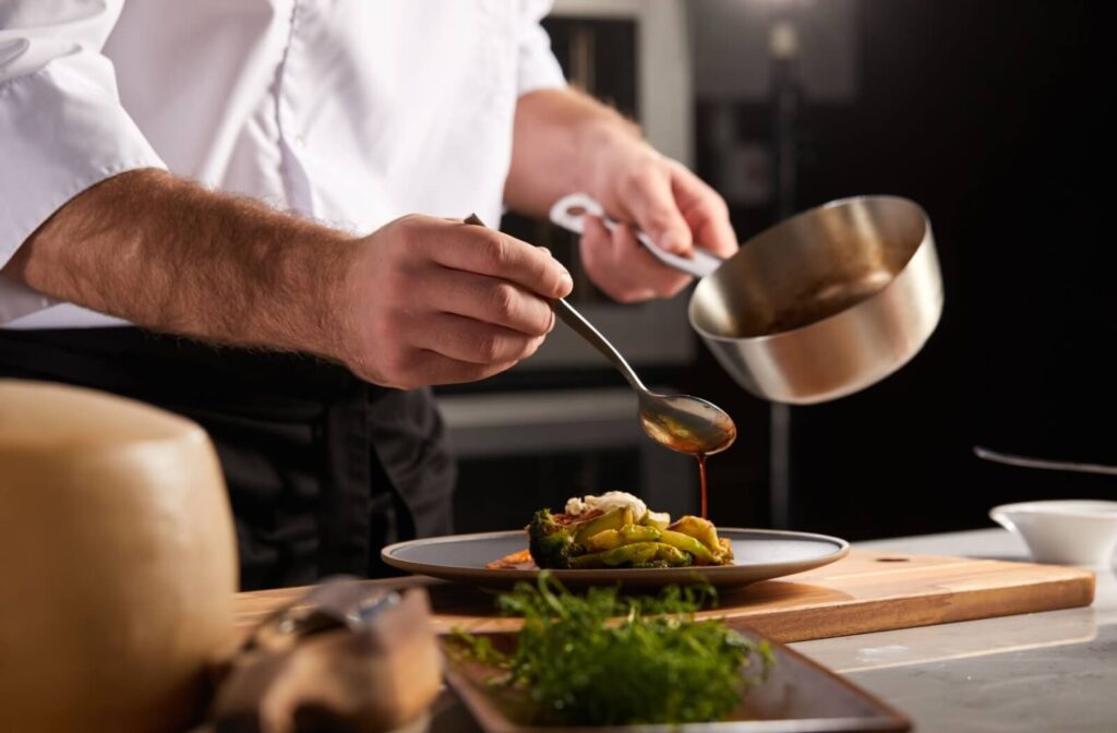 A chef in independent living drizzles sauce over a well-made plate of vegetables in a professional kitchen