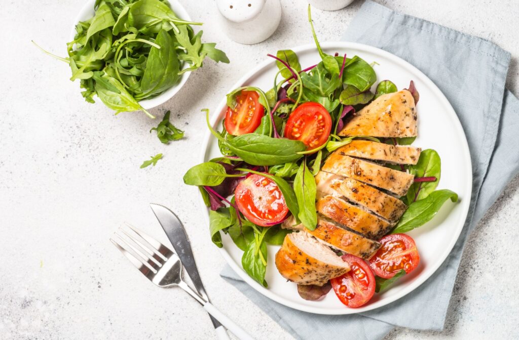 An overhead image of a sliced chicken breast laying on a fresh salad with tomatoes